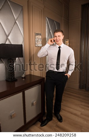 telephone conversation. successful handsome man in business clothes talking on the phone and smiling in chic interior. young man holding a phone in one hand and the other hand in his pocket