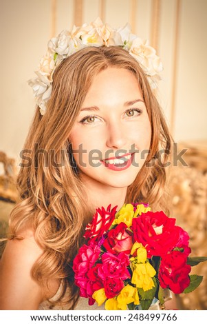 charming girl with flower wreath on head and with a bouquet in hands smiling.