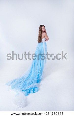 beautiful girl in a blue long dress with plume on a white background