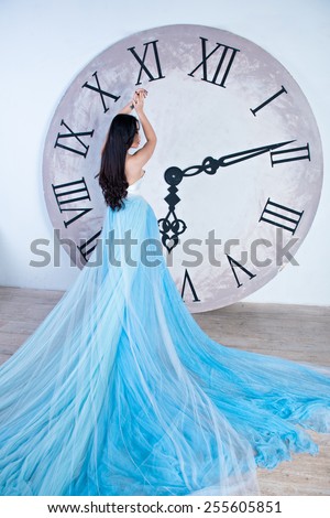 beautiful asian girl in a long dress with plume standing near the huge clock