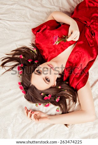 beautiful girl lying on the bed in a red robe. girl with flowers on head. charming girl with a flowers. young woman has a beautiful face.
