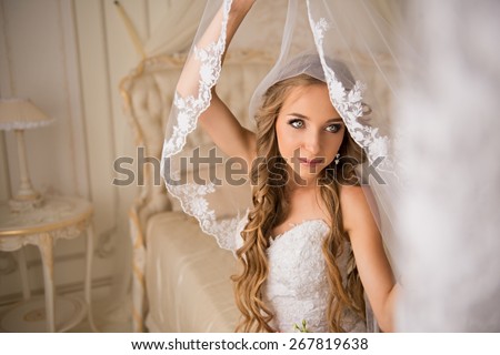 charming beautiful bride lifted her veil.  bride sitting on the bed in white dress in a luxury interior