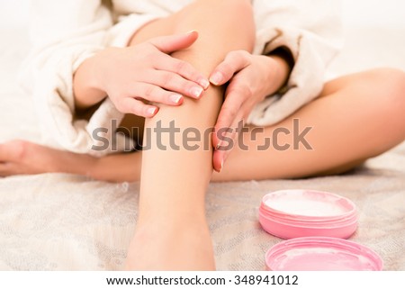Closeup photo of young woman smearing cream on her leg