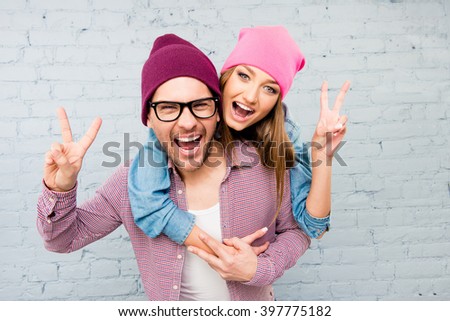 Happy cheerful man and woman embracing, gesturing with two fingers and screaming