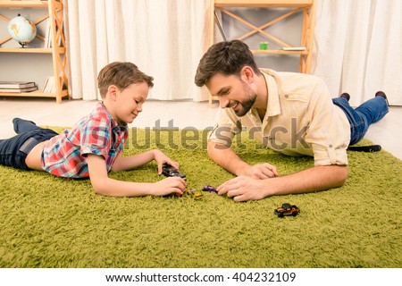 Father and son  lying on carpet and playing with toy cars