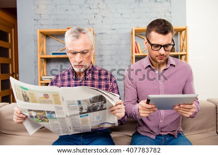 Old father reading newspaper and his son using tablet