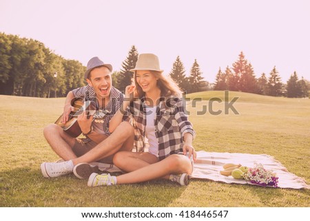 Happy couple in love having picnic in park with guitar