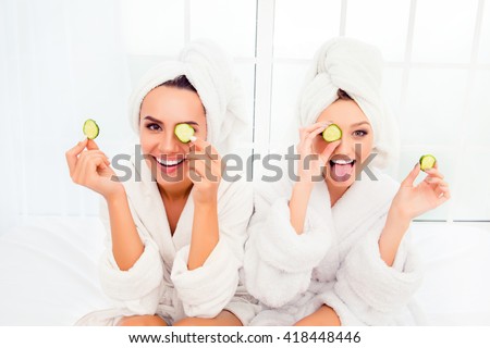 Comic young sisters after shower making mask with cucumber