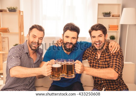 cheers! Handsome men celebrating victory of favorite team and clinking glass of beer at home