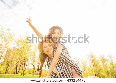 Cheerful happy woman piggybacking her pretty girlfriend