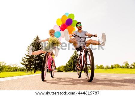 Happy funny young couple riding on bicycle with raised legs