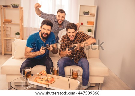 win! excited happy cheerful men play video game with beer and pizza at home