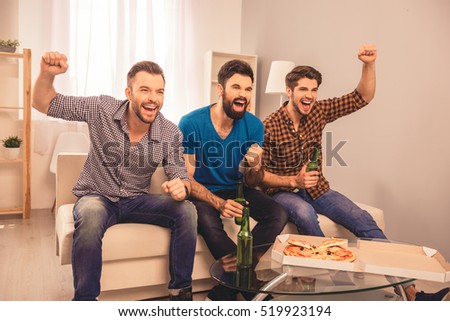 Portrait of three happy  men holding bottle of beer and watching tv