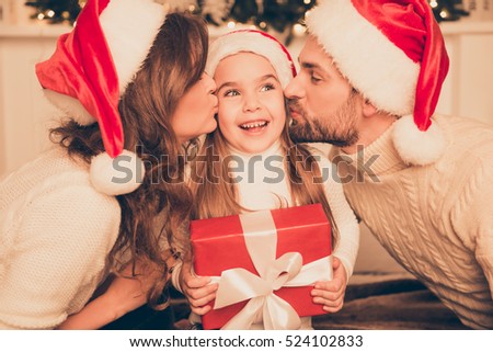 Happy parents kissing daughter and giving xmas present  on bed