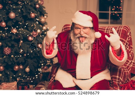 It\'s party! Cool Santa Claus showing tongue out and gesturing with fingers rock-and-roll near christmas tree at home