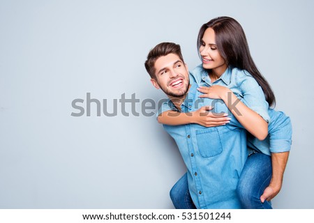Happy  man carrying his girlfriend on the back on gray background