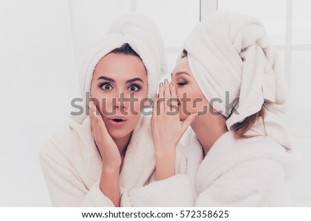 Portrait of young girl in bathrobe telling secret to her shocked sister.