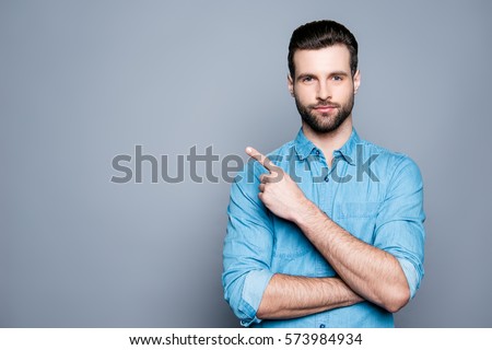 Handsome smiling bearded man pointing away on gray background.
