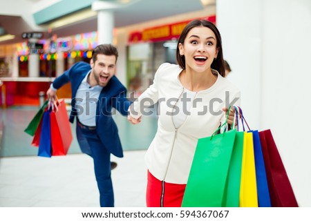 It\'s shopping and fun  time. Portrait of cheerful  successful happy young lovely couple holding  colored shopping bags and laughing in mall. Concept of consumerism, sale, rich life.