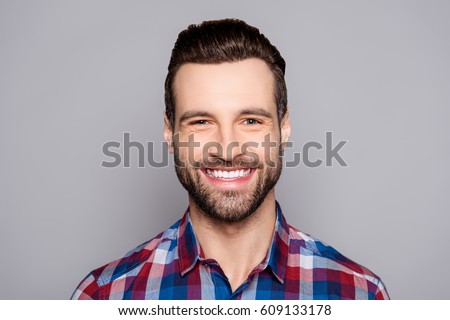 A close up portrait of young happy cheerful young man in checkered shirt in front of gray background.