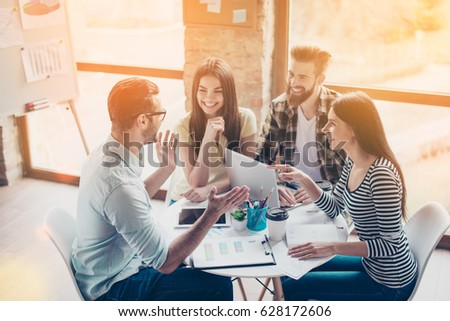 Cheerful partners are discussing an idea of new start-up by smiling and enjoying each others company in a light modern workplace