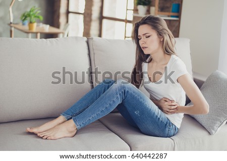 Sad beautiful woman sitting on the couch and feeling spasm and symptoms of pms