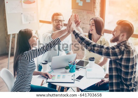 We did it! Four cheerful young people giving highfive to each other and smiling at the nice sunny day after they have done start up project together