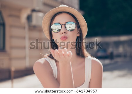 Kiss for you! Happy carefree girl on a holiday is sending an air kiss to her lover. She is in a fashionable hat and sunglasses