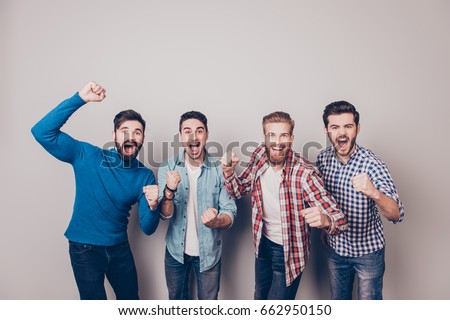 Champions! Four amazed young men are standing and gesturing for the victory on pure background in casual outfit and jeans. They are fans of sports games as football, basketball, hockey, baseball