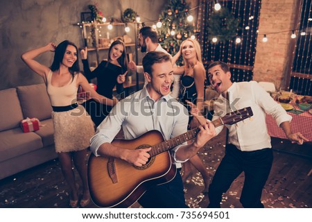 Celebrating newyear. Young handsome musician makes a noise with his instrument! Group of beautiful festive youth on luxury feast, many glitters on floor, classy outfits, Chilling relax mood all night