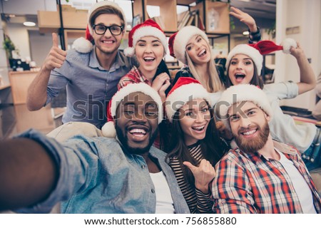 Self portrait of mixed race unity of african, american, asian, caucasian friends, happy bearded men and beautiful women in red santa hat showing thumb up, like, ok gesture to the camera in office