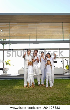 Six person family portrait in the backyard of a luxury house, gesturing thumbs up.