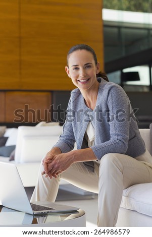 Smiling woman sitting in a sofa with laptop on coffee table. Close view.