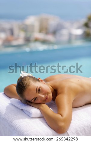 Young woman bare cheated lying on a massage table, with blue sea in the background.