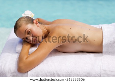 Young woman bare cheated lying on a massage table, with blue sea in the background.
