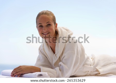 Portrait of a young woman wearing a white dressing gown and lying on a massage table.