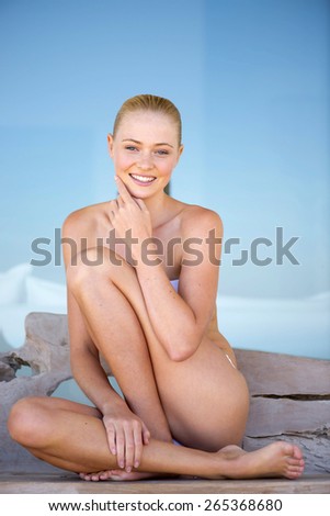 Beautiful young woman sitting with legs crossed and her hand on her chin over blue background.