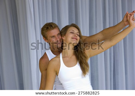 Young blond couple hand in hand and arms outstretched over net curtains background,