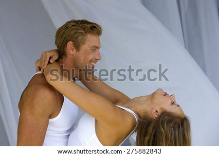 Young blond couple. Woman having her arms around the man\'s neck. Net curtains background,