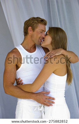 Young blond couple kissing over net curtains background,