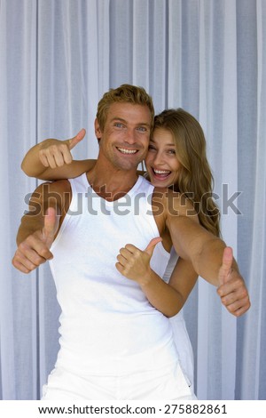 Young blond couple gesturing thumbs up over  net curtains background,