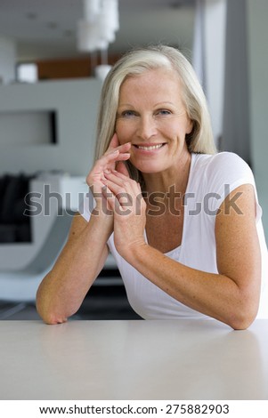 Portrait of senior woman leaning on a table with clasped hands.