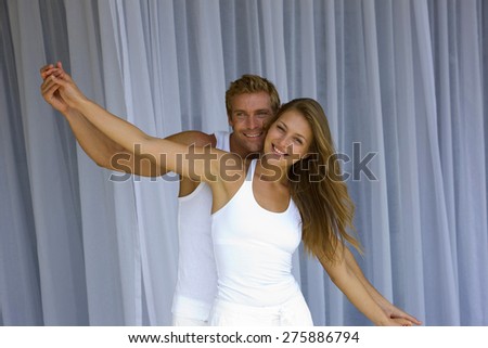Young blond couple hand in hand and arms outstretched over net curtains background,