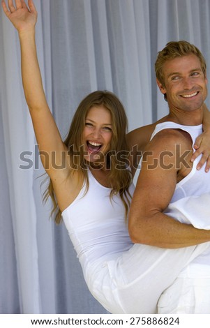Young blond couple. The young man is carrying the young girl on his back. The girl is laughing and raising one harm.