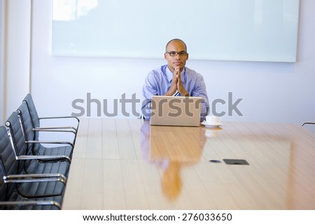 Business manager sitting at the end of a meeting table, with cup of cafe and laptop, thinking.