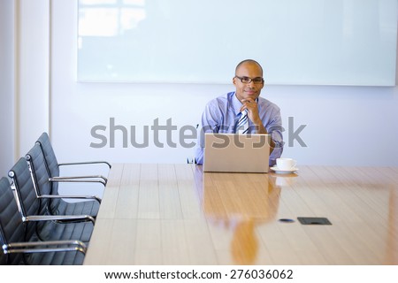 Smiling business manager sitting at the end of a meeting table, with cup of cafe and laptop.