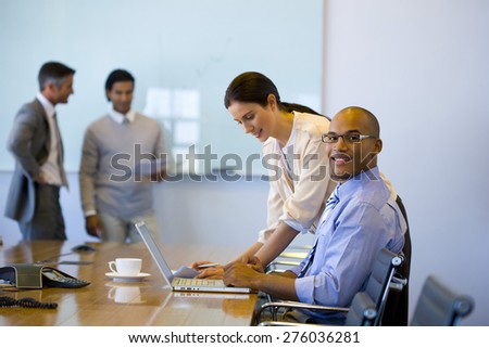 Male and female executives working together in a meeting room with trainer using white board in the background.