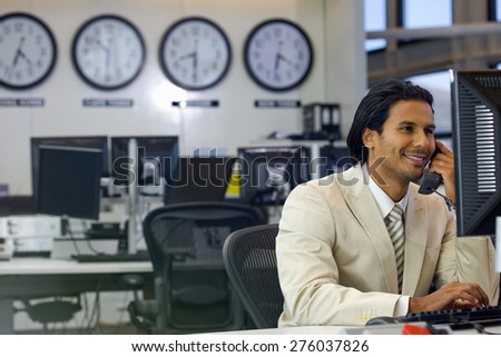 Business executive on the phone in open space office with time zone clocks in the background.