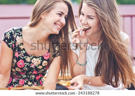 Two young female friends laugh and eat chocolate outdoors