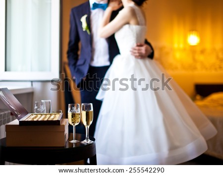 Just married couple, champagne and box of chocolates near a window. Groom embraces bride. Focus on champagne in front of couple